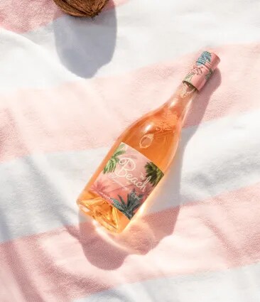 The Beach rosé bottle placed on striped cloth with sunlight and tropical details