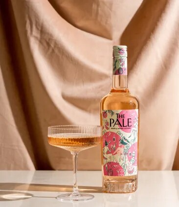 The Pale rosé bottle and glass on a table with soft draped fabric background
