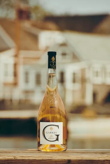 Bouteille de rosé Garrus posée sur une table avec un bâtiment du domaine en arrière-plan