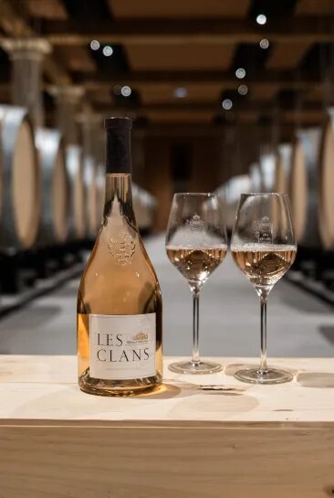 Bouteille de rosé Les Clans avec deux verres sur une table dans le chai