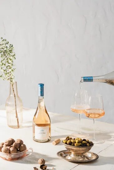 Château d’Esclans rosé being poured into glasses with olives and nuts on a table