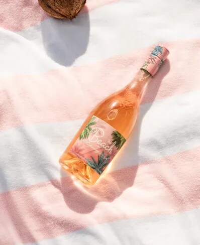 The Beach rosé bottle placed on striped cloth with sunlight and tropical details