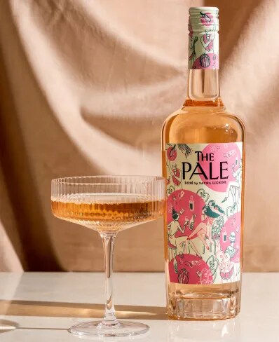 The Pale rosé bottle and glass on a table with soft draped fabric background